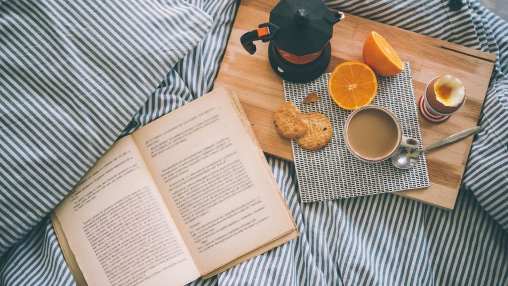 Carte de dezvoltare personală pe masă alături de o ceașcă de cafea și un mic dejun servit pe o masă de lemn, invitând la o dimineață de lectură înțeleaptă și relaxare.