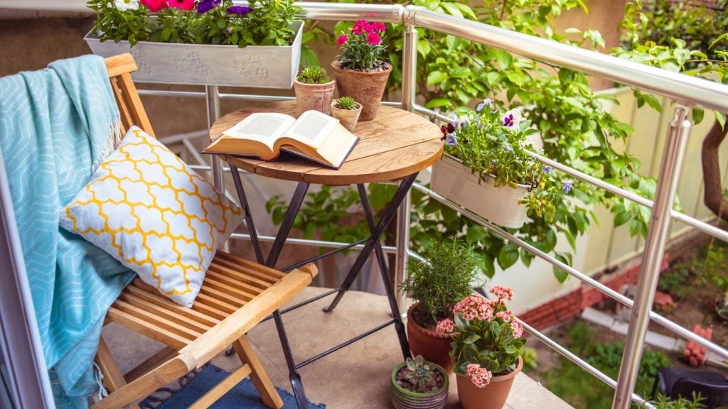 Terasă de vară cozy, scaun, masă, multe plante în jur și o carte de beletristică pe masă, un colț de lectură ideal