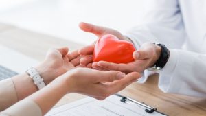 Vedere Detaliată a Unui Doctor și a Unui Pacient Ținând În Mâini o Inimă Roșie, Concept de Asigurare Medicală: Această imagine simbolizează importanța îngrijirii sănătății și a prevenției, aspecte esențiale menționate în multe cărți despre sănătate. Ea reprezintă legătura dintre pacienți și medici și importanța dialogului și a înțelegerii reciproce pentru o sănătate optimă.