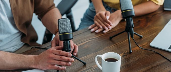 Gazde de podcasturi românești în studio: Fotografia surprinde doi creatori de podcasturi românești, concentrați și angajați într-o discuție captivantă, înconjurându-se de microfoane profesionale. Această imagine reflectă esența procesului de creare a unui podcast în România, punând în lumină interacțiunea și profesionalismul ce stau la baza unor producții audio de succes în spațiul românesc.