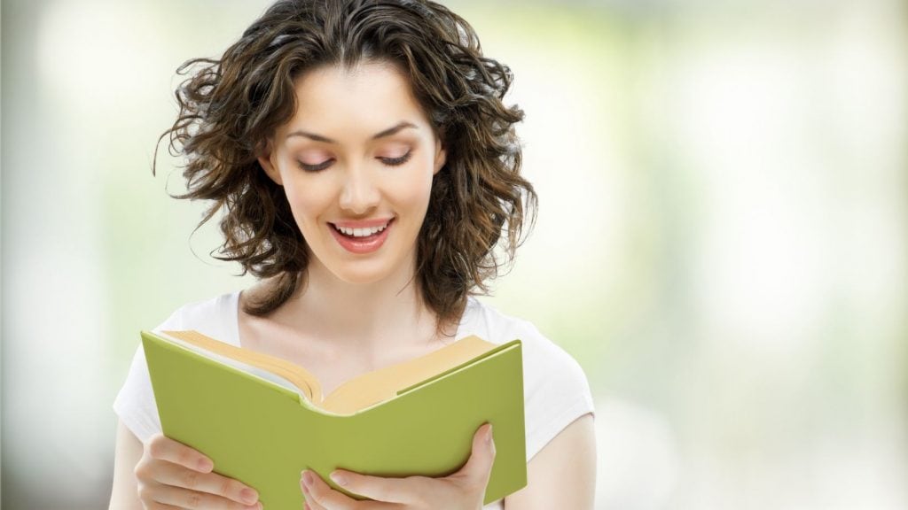 Femeie frumoasă zâmbitoare citind o carte: O imagine plină de căldură și bucurie, cu o femeie atrăgătoare care citește o carte. Imaginea surprinde o femeie în timp ce citește o carte mare, ilustrând pasiunea pentru literatură și dorința de a descoperi rezumate captivante de cărți.
