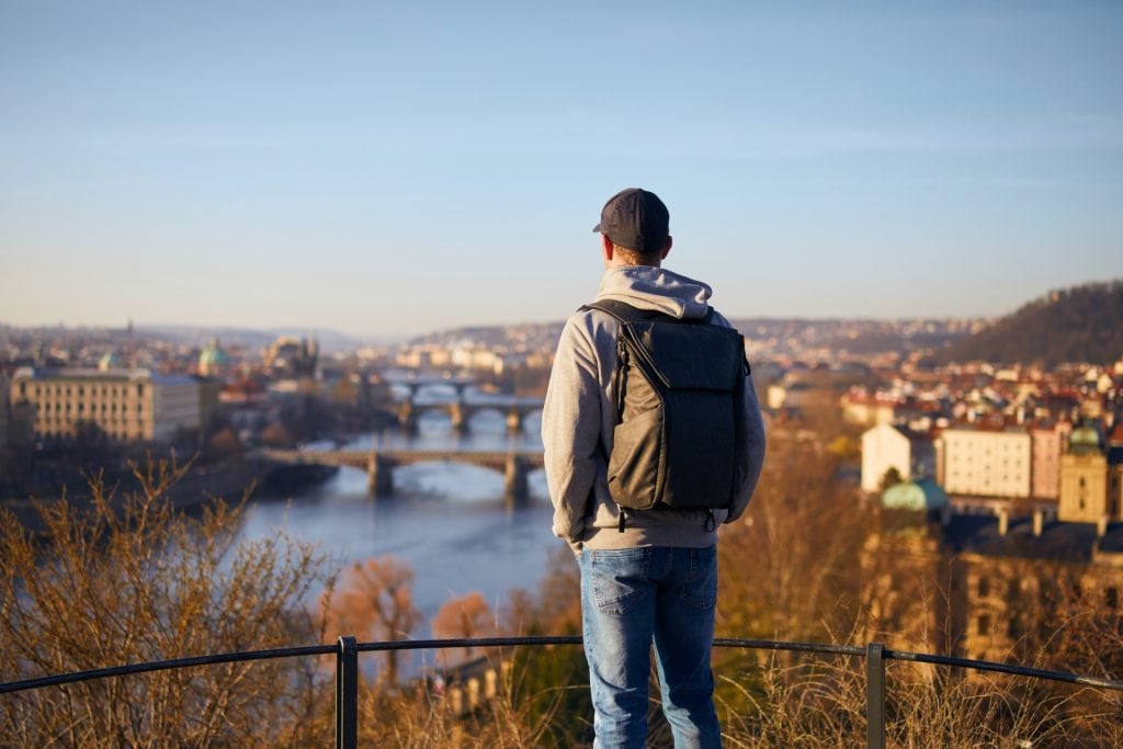 Turist privind panorama orașului Praga cu podurile sale pitorești în timpul unui city break last minute, subliniind oportunitățile de călătorii de ultim moment.