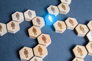 Imagine conceptuală prezentând numeroase hexagoane din lemn cu figuri umane, concentrate în jurul unui hexagon albastru luminos cu o figură umană albă, simbolizând dezvoltarea profesională durabilă și leadership-ul într-un grup.