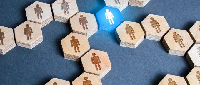 Imagine conceptuală prezentând numeroase hexagoane din lemn cu figuri umane, concentrate în jurul unui hexagon albastru luminos cu o figură umană albă, simbolizând dezvoltarea profesională durabilă și leadership-ul într-un grup.