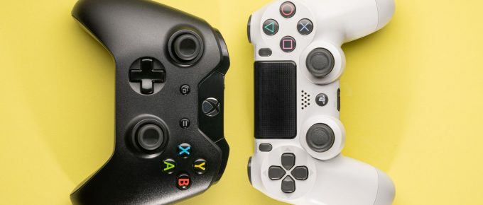 Controlere de gaming pentru console jocuri video, ilustrând un controller Xbox negru și un controller PlayStation alb pe un fundal galben, reprezentând diversitatea opțiunilor pentru jucători.