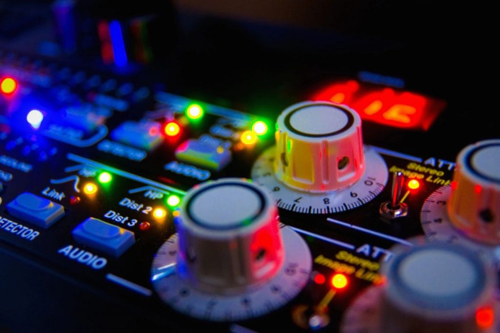 Mixer audio profesional cu multiple fadere, butoane și rotițe pentru reglarea volumului și efectelor sonore, evidențiind detaliile tehnice ale echipamentului.