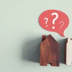 Două modele stilizate de case, una mare din lemn închis la culoare și una mai mică, din lemn alb, plasate pe un fundal pastelat. Deasupra acestora este o bulă de dialog roșie cu semne de întrebare albe, sugerând nesiguranță sau îndoială de sine. Aceasta ar putea simboliza dilemele sau incertitudinile legate de alegeri sau decizii de viață importante.