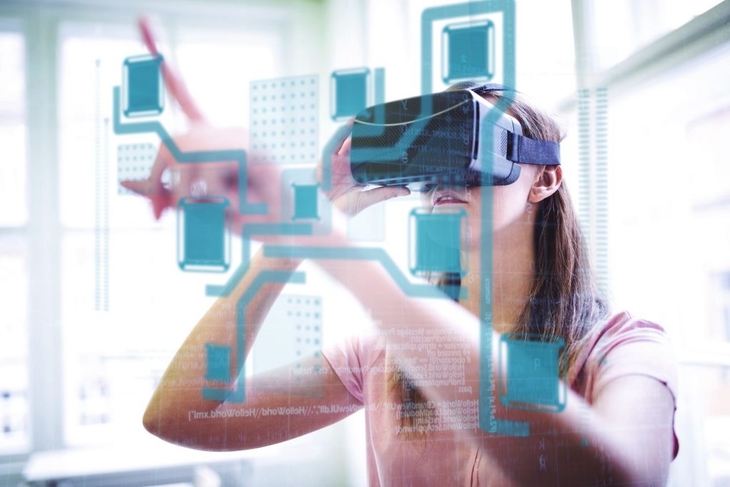 O persoană interacționează cu o interfață digitală folosind ochelari VR de realitate virtuală, grafica suprapusă indicând posibil un proces de învățare sau manipulare de date într-un mediu virtual. Lumina naturală și decorul urban din fundal contrastează cu elementele digitale, sugerând o fuziune între spațiul fizic și cel virtual.