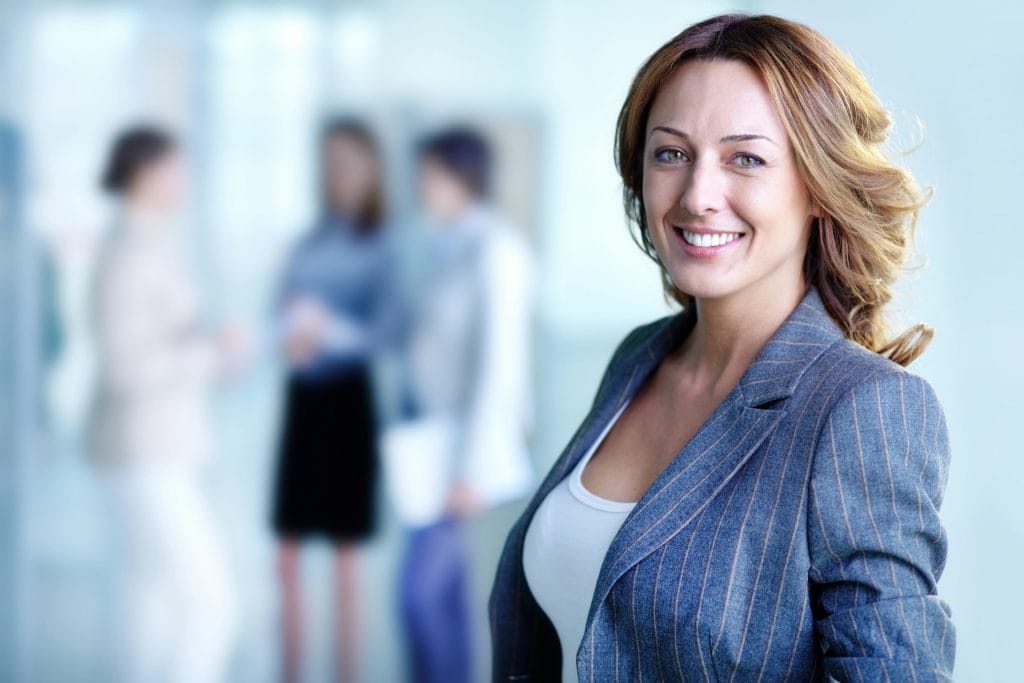 Femeie de afaceri încrezătoare stând în birou cu colegi în fundal, reprezentând stima de sine profesională